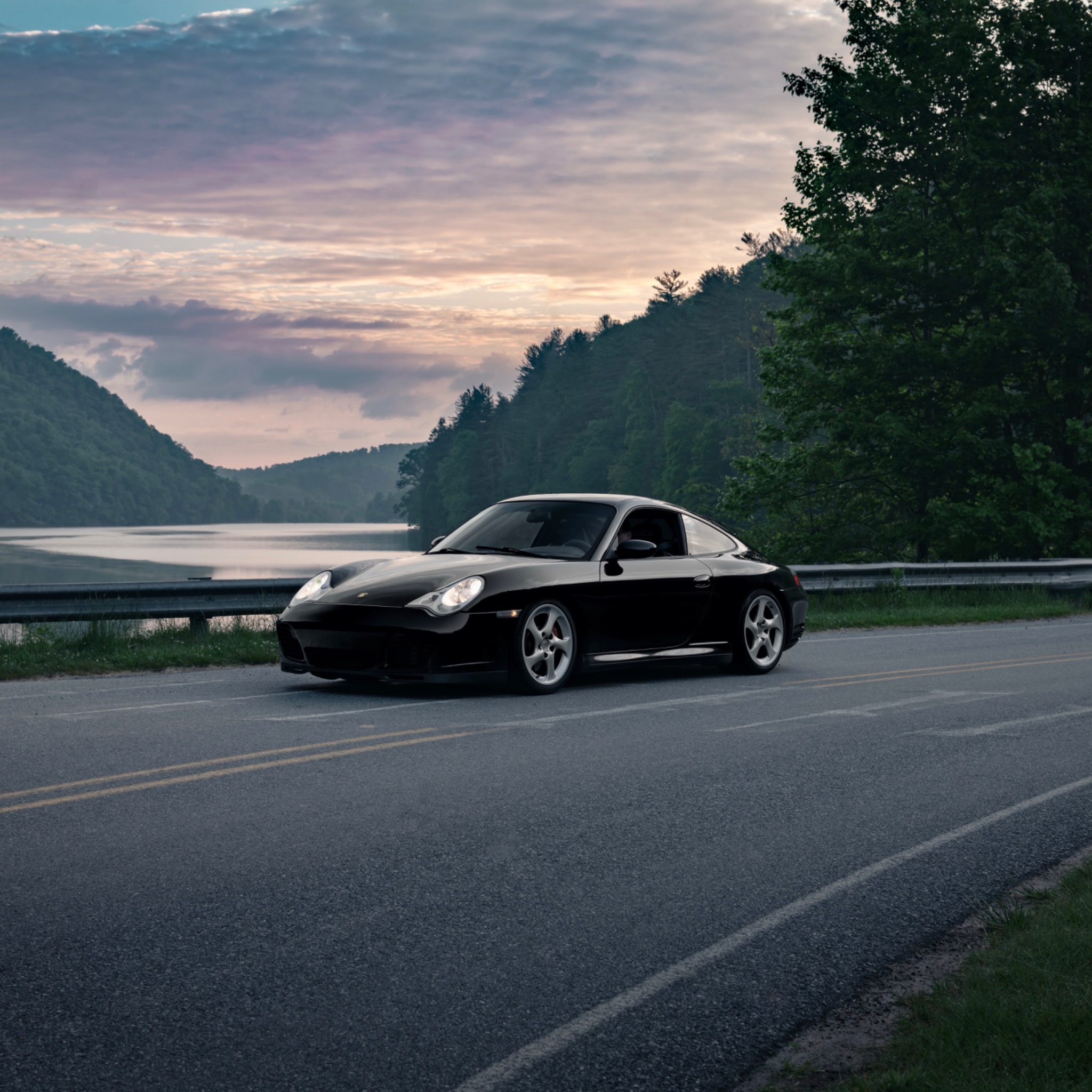 A 996 Carrera at dusk on a lakeside road - the 996.1 silhouette is unmistakable in any light.